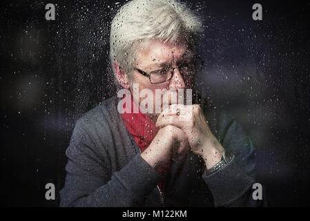 L'homme triste à menton reposant sur des mains à la fenêtre avec des gouttes de pluie close up Banque D'Images