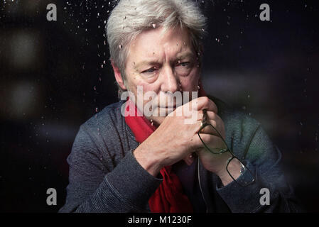 L'homme inquiet à la suite holding glasses devant faire face à la fenêtre avec des gouttes de pluie close up head shot Banque D'Images