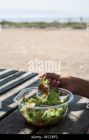 Libre d'un jeune homme de race blanche de manger une salade préparée assis à une table en bois à l'extérieur à l'ombre Banque D'Images