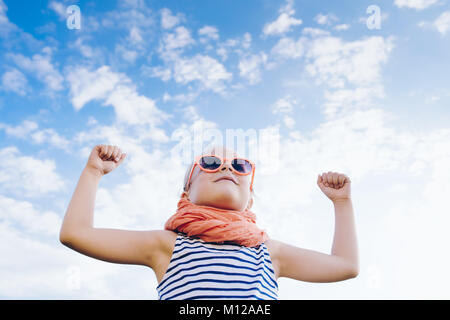 Happy child girl à lunettes avec mains ouvertes contre le fond de ciel Banque D'Images