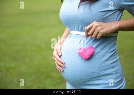 Le portrait d'une femme enceinte en robe bleue la tenue d'une seule forme de coeur accessoires Banque D'Images