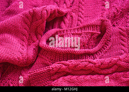 La main à la main, de couleur rose vif en tricot pull en coton avec un câble unique. Banque D'Images