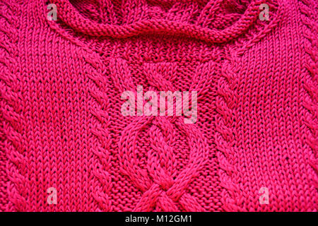La main à la main, de couleur rose vif en tricot pull en coton avec un câble unique. Banque D'Images