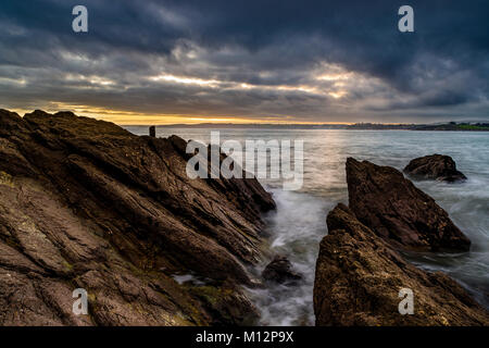 Un arbre de lumière des particules de l'autre côté de la mer agitée et anxieuse skys dans Polkerris. Banque D'Images