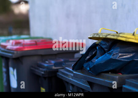 Ligne de débordement des poubelles avec des couvercles de couleurs différentes et sacs noirs de refuser. Banque D'Images