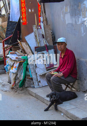 Beijing, Chine - pas de personnes âgées Chinese man et son chien est assis sur le côté d'une rue étroite dans la ville, de l'image en format portrait Banque D'Images