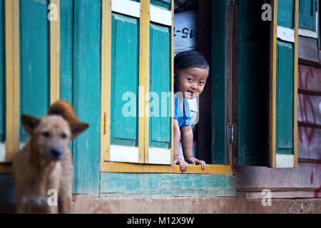 Jeune garçon dans un village du nord du Laos est à la recherche à travers une vitre, l'Indochine, l'Asie Banque D'Images