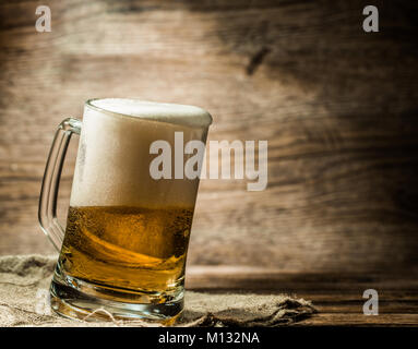 La bière mousseuse versée dans la tasse debout sur une table en bois Banque D'Images