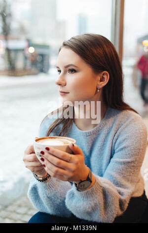 Portrait de jeune fille tenir tasse à café et regarder la caméra. Porter des vêtements élégants. L'automne et l'hiver. Arrière-plan flou. Photo Proffesional. Banque D'Images