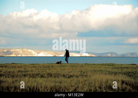 Portland, UK. 26 janvier 2018 - Un homme promène son chien autour de chilly Portland Harbour, prendre le soleil au-delà des falaises jurassiques Crédit : Stuart fretwell/Alamy Live News Banque D'Images