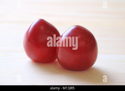 Fermé une paire de couleur rouge rubis du golfe mûrs Fruits Prunes isolé sur table en bois Banque D'Images