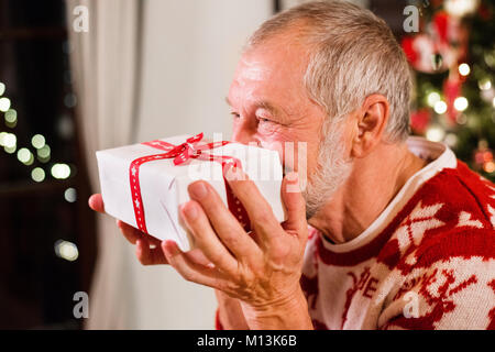 Senior man in front of Christmas Tree tenant un cadeau. Banque D'Images