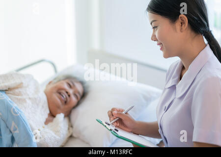 Infirmière asiatique de l'histoire de la maladie patient âgé au lit. Infirmière s'occupe d'une femme âgée. Banque D'Images