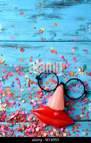 Portrait d'une paire de lunettes noires, un faux nez et une bouche formant le visage d'une personne sur une surface en bois rustique bleu plein de confetti Banque D'Images