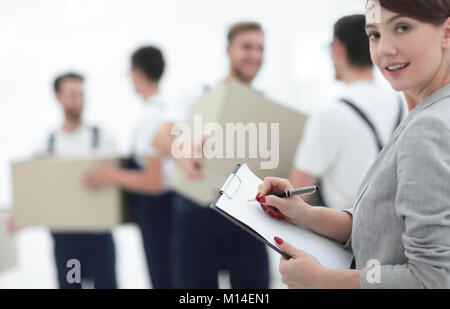 Femme manager holding clipboard sur fond flou avec des déménageurs et des boîtes. Banque D'Images