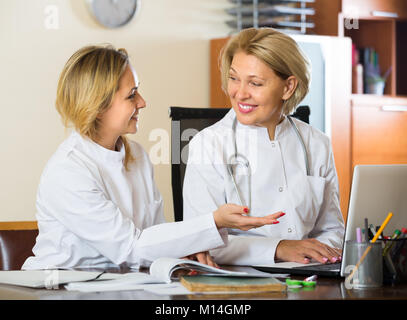 Portrait of two female doctors en combinaisons blanches doing paperwork at clinique. Selective focus Banque D'Images