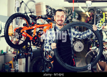 Jeune homme en tablier tenant une roue de vélo dans un magasin de vélos Banque D'Images