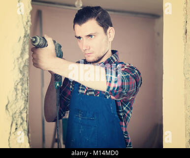 Constructeur professionnel calme de percer le trou dans le mur avec une perforatrice dans chambre réparables Banque D'Images