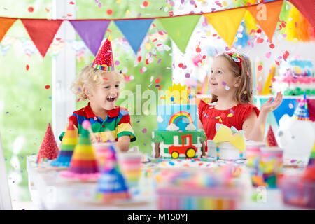 Kids Birthday party. Enfant blowing out candles on cake coloré. Maison décorée avec des bannières drapeau arc-en-ciel, de ballons, de confettis. Les transports et la ferme Banque D'Images