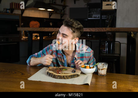 Personne affamée émotionnellement consomme des aliments sur le petit-déjeuner. Jeune homme assis à la table de la cuisine à la maison moderne. Beau gars tôt le matin Banque D'Images