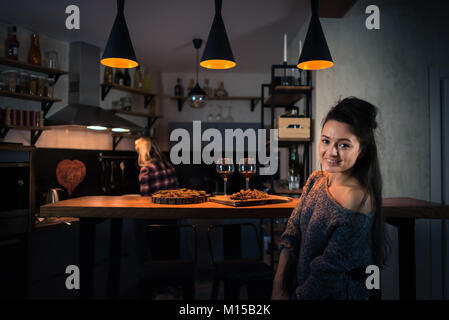 Les jeunes femmes à préparer le dîner dans la soirée. Blonde d'un séjour retour sur l'arrière-plan. L'alimentation et du vin sur le comptoir du bar. Coeur peint sur le mur Banque D'Images