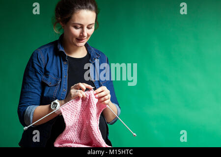 Jeune femme en chemise en jean tricote avec chandail tricoté à partir de laine naturelle fil de couleur rose sur fond vert isolés Banque D'Images