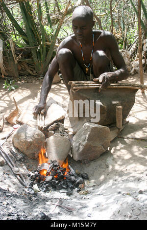 Homme de Datoga prépare et allume le feu de camp à l'aide d'une peau de chèvre d'un soufflet. Photographié en Afrique du Sud, la Tanzanie, le lac Eyasi Banque D'Images