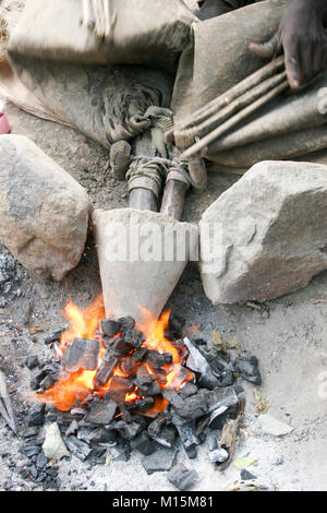 Homme de Datoga prépare et allume le feu de camp à l'aide d'une peau de chèvre d'un soufflet. Photographié en Afrique du Sud, la Tanzanie, le lac Eyasi Banque D'Images