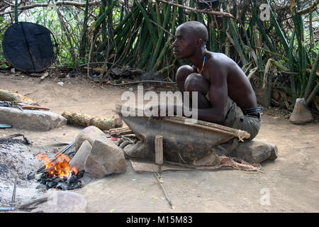 Homme de Datoga prépare et allume le feu de camp à l'aide d'une peau de chèvre d'un soufflet. Photographié en Afrique du Sud, la Tanzanie, le lac Eyasi Banque D'Images