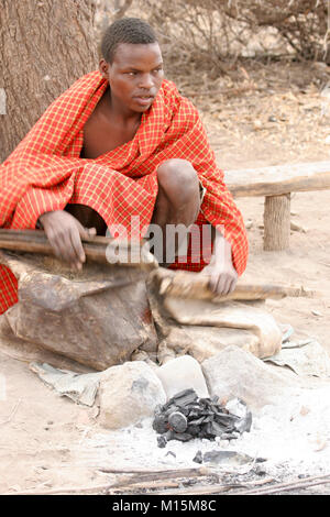 Homme de Datoga prépare et allume le feu de camp à l'aide d'une peau de chèvre d'un soufflet. Photographié en Afrique du Sud, la Tanzanie, le lac Eyasi Banque D'Images