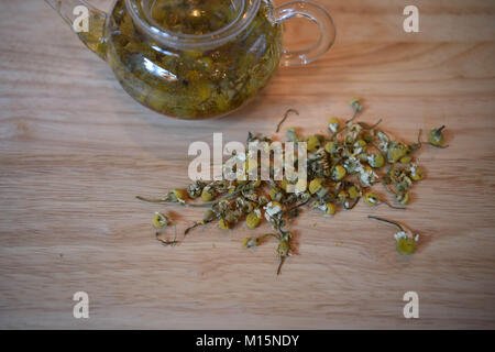 Photographie d'une boisson fraîche ou chaude saine camomille camomille thé dans une théière en verre avec des feuilles florales sur un fond de table en bois clair Banque D'Images