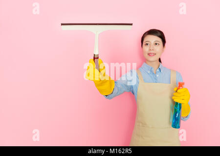 Belle jeune femme de ménage debout dans fond rose lave-vitre et à l'aide d'essuie-glace en verre détergent de nettoyage de la mousse. Banque D'Images