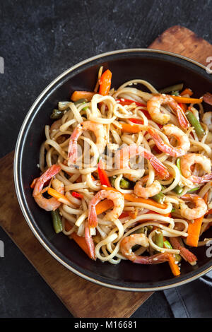 Faire revenir avec les nouilles Udon, crevettes (crevettes) et de légumes. La nourriture saine, de l'Asie, repas sautés au wok sur fond noir, copiez l'espace. Banque D'Images