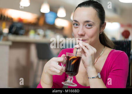 Happy young girl in red dress de boire le vin chaud assis dans un café Banque D'Images