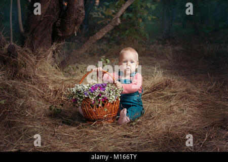 Petite fille assise dans la forêt avec un panier de fleurs. Banque D'Images