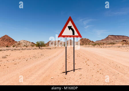 Un panneau routier indiquant un virage à gauche, à côté d'une route de gravier dans le nord de la Namibie. Banque D'Images
