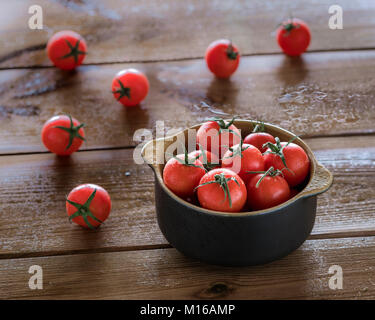 Tomates Cocktail vaporisé avec de l'eau dans la cuvette sur table en bois brun Banque D'Images