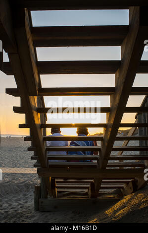 Couple de touristes aîné assis sur l'escalier en bois et profiter de la magnifique lever du soleil. Islantilla, Huelva, Espagne Banque D'Images
