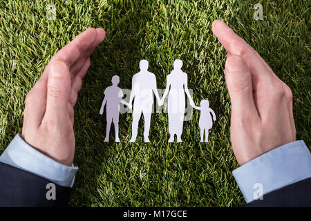 View of a person's hand protection Family Paper Cut Out On Green Grass Banque D'Images
