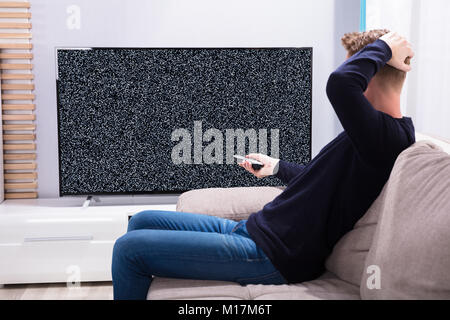 Homme assis sur le canapé en regardant la télévision avec aucun signal Banque D'Images