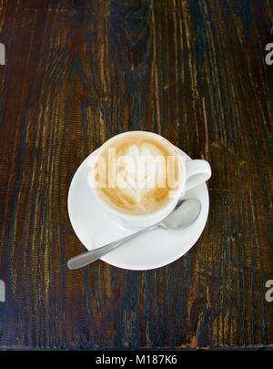 Télévision avec café blanc motif dans la mousse avec une cuillère sur fond de bois foncé Banque D'Images