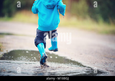 La marche de l'enfant dans la flaque en wellies sur temps de pluie Banque D'Images
