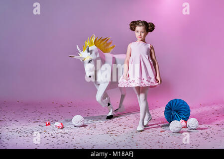 Petite fille romantique dans une belle robe rose. L'origami et le minimalisme. Les enfants de la mode. Designer collection. Gros blanc en papier origami UNICORN. Banque D'Images