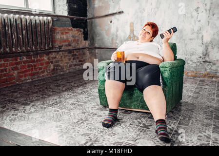 L'excès de woman sitting in chair et boit de la bière, des calories des aliments, de l'obésité. Mode de vie malsain, femelle gras Banque D'Images