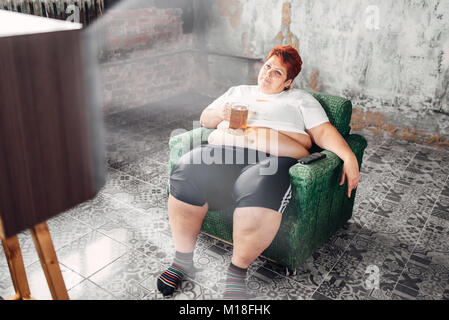 L'excès de woman sitting in chair et boit de la bière, l'obésité, boulimiques. Mode de vie malsain, femelle gras Banque D'Images