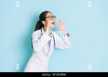 Femme médecin assez attirantes avec les mains comme à haut-parleur au-dessus de zone vide criant isolé sur fond bleu. Banque D'Images