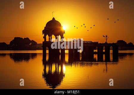 Gadisar lake (Gadi Sagar) Jaisalmer Rajasthan avec ancien temple d'architecture en silhouette au lever du soleil. Banque D'Images