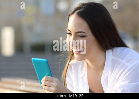 Portrait d'un ado smiley à l'aide d'un smart phone bleu sur rue Banque D'Images