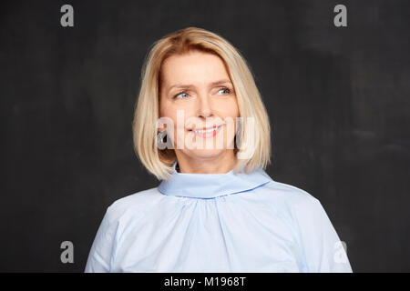Portrait d'une belle mature woman posing at fond sombre tout en souriant et à la voiture. Banque D'Images