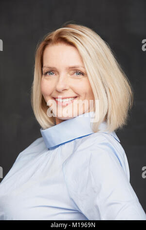 Close-up portrait of a beautiful young woman posing at fond sombre tout en souriant et en regardant la caméra. Banque D'Images